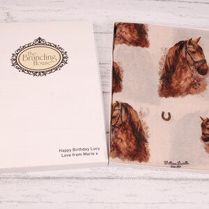 Puede incluir: Una caja de regalo blanca con una bufanda de estampado de caballo marr&oacute;n en su interior. La caja tiene un logotipo que dice "The Branding House" y un mensaje que dice "Happy Birthday Lucy Love from Marie x". La bufanda tiene un estampado de caballo marr&oacute;n con un dise&ntilde;o de herradura.