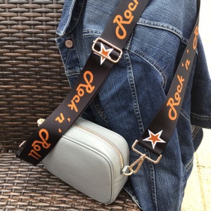 May include: A gray crossbody bag with a black and orange adjustable strap that says "Rock 'n' Roll".