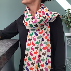 May include: A white scarf with a colorful rabbit print. The rabbits are in various colors, including red, orange, yellow, green, blue, and purple.