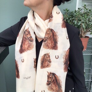 Puede incluir: Una bufanda blanca con un estampado de caballo marr&oacute;n y un dise&ntilde;o de herradura. La bufanda presenta un patr&oacute;n repetido de caballos y herraduras. El texto "William P. Bella" est&aacute; impreso en la bufanda.