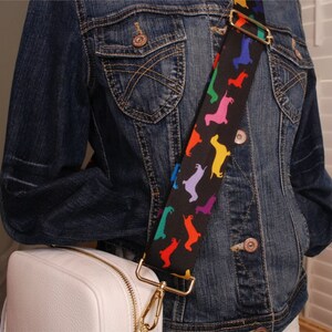 May include: A white leather crossbody bag with a gold chain strap. The strap is decorated with a black and white pattern of colorful dachshund silhouettes.