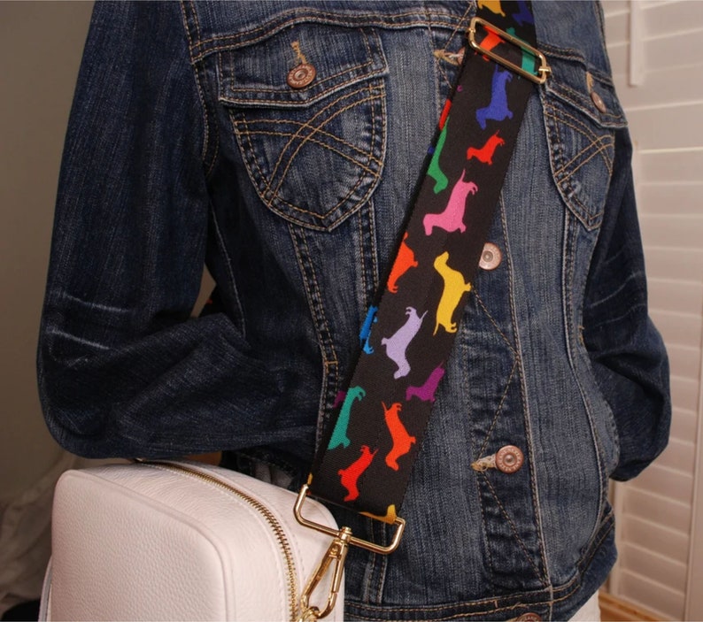 May include: A white leather crossbody bag with a gold chain strap. The strap is decorated with a black and white pattern of colorful dachshund silhouettes.