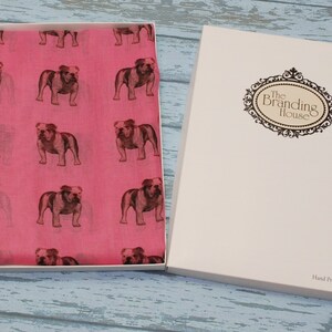 May include: A pink scarf with a repeating pattern of brown bulldog silhouettes. The scarf is in a white box with the text "The Branding House" on the lid. The bottom of the box says "Hand Printed in the UK."