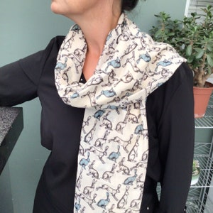 May include: A white scarf with a pattern of blue and brown rabbits. The scarf is worn around the neck of a person wearing a black shirt.