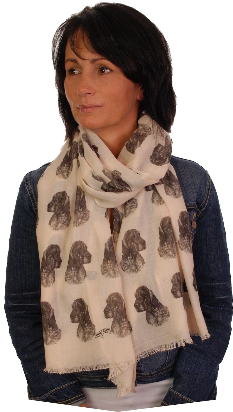 May include: A cream-colored scarf with a repeating pattern of brown and black dog heads. The scarf has a fringed edge and the text "Mikey's Designs" is printed on the bottom right corner.