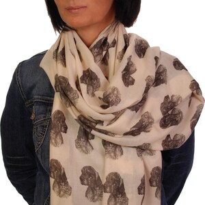 May include: A woman wearing a denim jacket and a cream-colored scarf with a repeating pattern of brown and white dog heads.