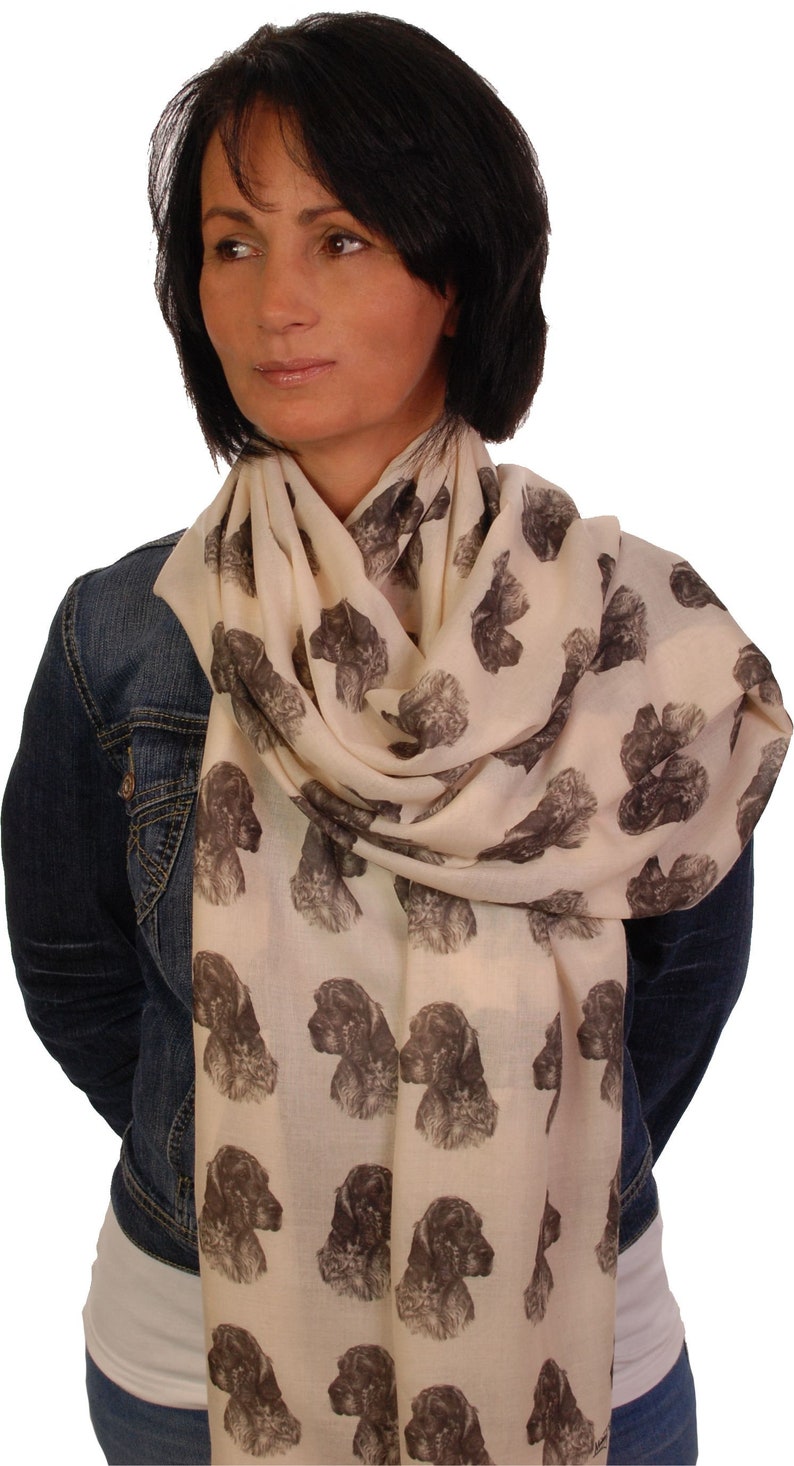 May include: A woman wearing a denim jacket and a cream-colored scarf with a repeating pattern of brown and white dog heads.