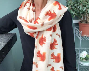 May include: A white scarf with a repeating pattern of red squirrels and acorns. The scarf is made of a soft, lightweight fabric and is perfect for adding a touch of whimsy to any outfit.