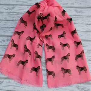 May include: A bright pink scarf featuring a repeating pattern of dark brown and black husky dog silhouettes. The lightweight fabric has a soft texture and finished edges with a delicate fringe detail along the bottom hem of the rectangular accessory.