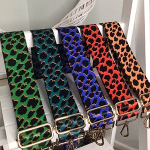 Pode incluir: Cinco correias ajustáveis com estampa de leopardo e ferragens douradas. As correias são verde, azul-esverdeado, azul, laranja e marrom.