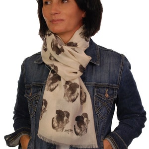 May include: A woman wearing a denim jacket and a beige scarf with a black and white border collie print. The scarf has a fringe edge and the text "Border Collie" printed on it.