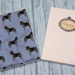 May include: A light blue fabric featuring a repeating pattern of dark gray and white husky dogs, presented in an open rectangular box. The box lid is white with a decorative black oval frame containing the text The Branding House.