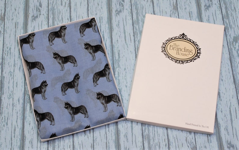 May include: A light blue fabric featuring a repeating pattern of dark gray and white husky dogs, presented in an open rectangular box. The box lid is white with a decorative black oval frame containing the text The Branding House.