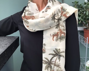 May include: A white scarf featuring a design of palm trees and leopards. The scarf is worn around a person's neck.