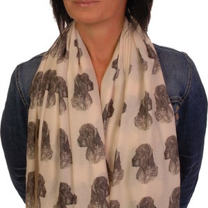 May include: A cream-colored scarf with a repeating pattern of brown and white dog heads. The scarf is worn by a person with dark hair.