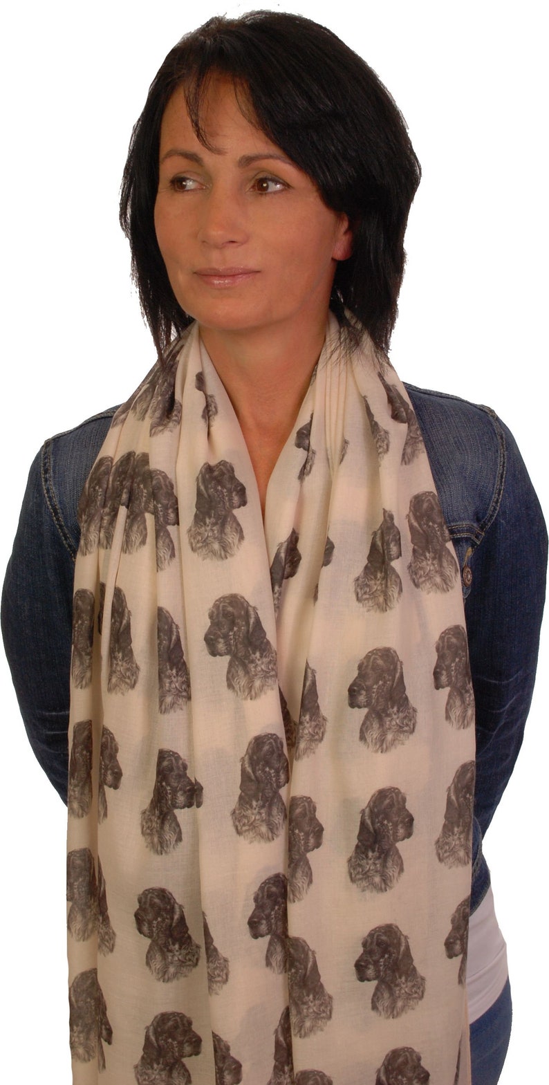 May include: A cream-colored scarf with a repeating pattern of brown and white dog heads. The scarf is worn by a person with dark hair.