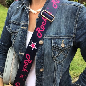 May include: A blue and pink adjustable camera strap with a white star and the text "Rock 'n' roll" in pink lettering.