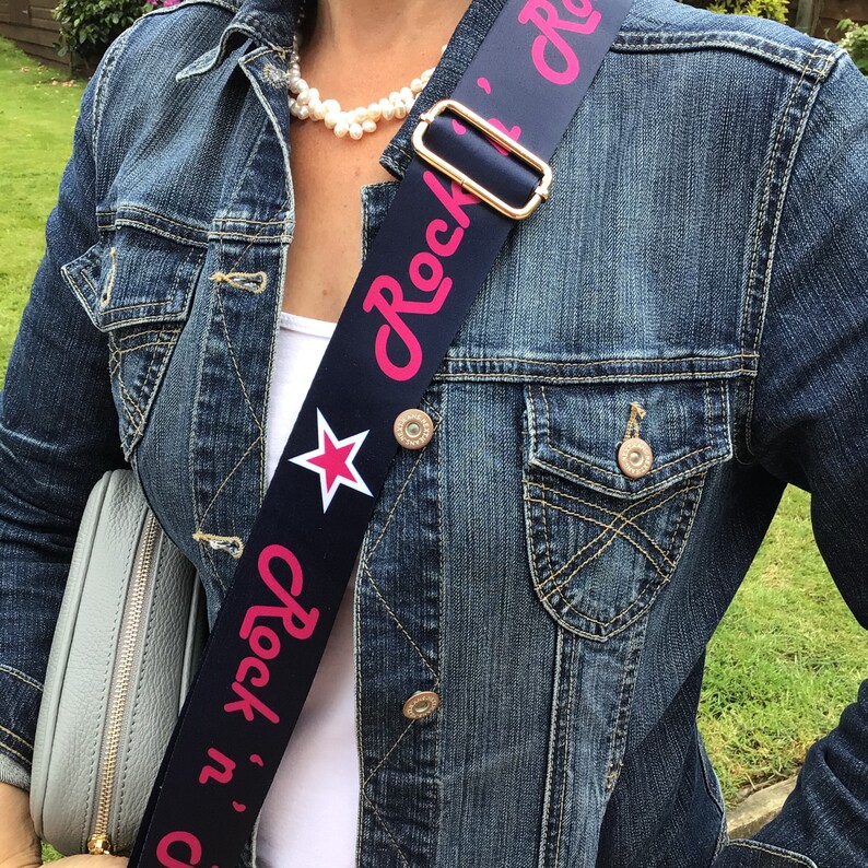 May include: A blue and pink adjustable camera strap with a white star and the text "Rock 'n' roll" in pink lettering.