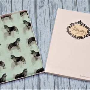 May include: A light green fabric scarf featuring a repeating pattern of dark gray husky dogs, presented in an open rectangular box. The box lid is cream-colored with a decorative black oval frame containing the text The Branding House.