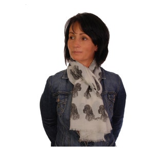 May include: A white scarf with a black and white print of a dog's face. The scarf is worn by a person wearing a denim jacket.