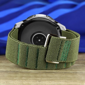 May include: A green and silver smartwatch band with a textured fabric design. The band is made of a soft, comfortable material and has a secure buckle closure.