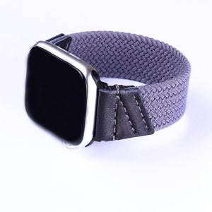 Puede incluir: Una banda para Apple Watch gris y negra con una correa de tejido tejido y una hebilla de cuero negro.