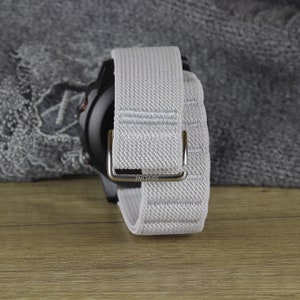 May include: A gray and white woven watch band with a silver buckle. The buckle has the word "SDVLINE" engraved on it.