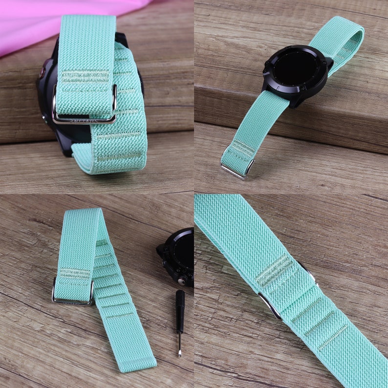 Puede incluir: Una correa de reloj de nylon azul claro con una hebilla plateada. La correa se muestra sobre una superficie de madera y en un reloj inteligente negro.