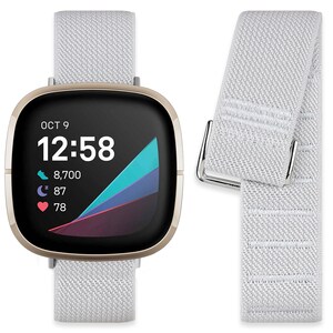 May include: A gold-colored smartwatch with a white woven band. The watch face displays the date, time, steps, sleep, and heart rate. The watch is shown next to a spare white woven band.