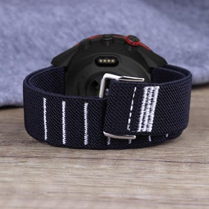 May include: Black and white striped elastic watch strap with a silver buckle. The strap is designed for a smartwatch with a black and red case.