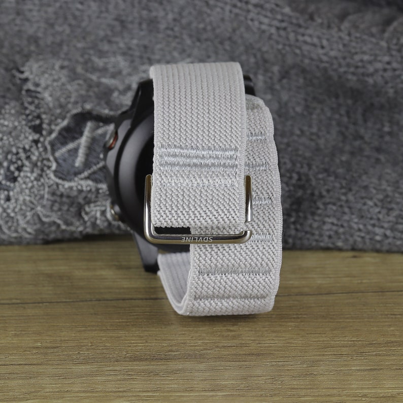 May include: A gray and white woven watch band with a silver buckle. The buckle has the word "SDVLINE" engraved on it.