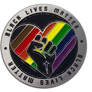May include: A silver-colored coin with a black heart design. The heart is filled with rainbow stripes and a black fist. The coin is surrounded by the text "Black Lives Matter" in a circle.