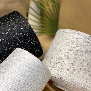 May include: Three spools of yarn with sequins. The yarn is white, black, and white with multi-colored sequins.