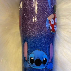Pu&ograve; includere: Un bicchiere glitter viola e blu con un personaggio di Stitch di Lilo & Stitch e un personaggio di Lilo di Lilo & Stitch sul lato.