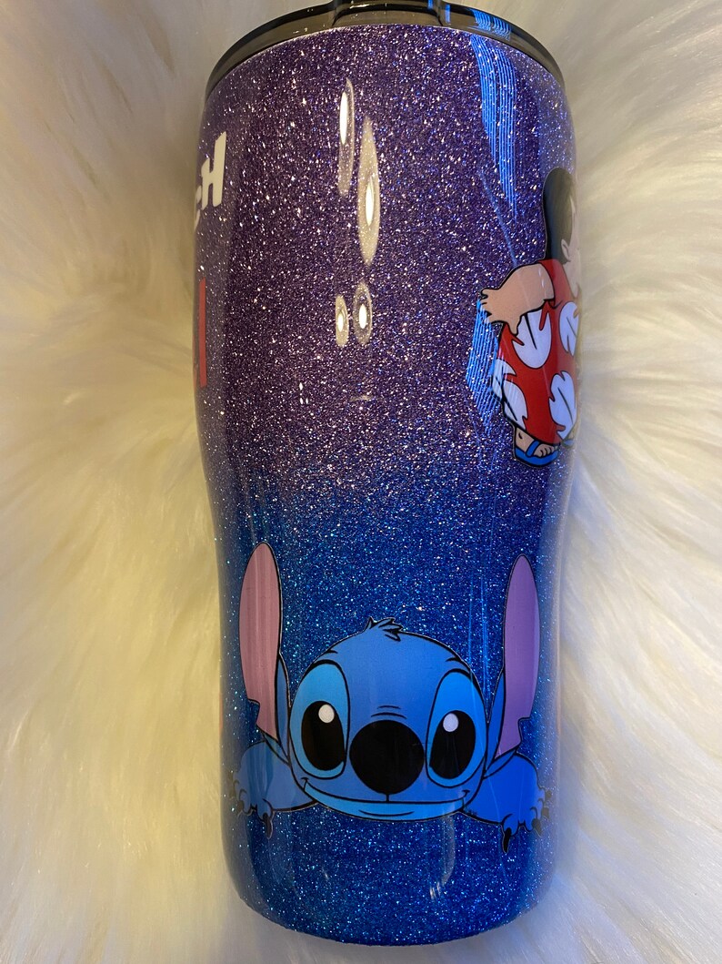 Pu&ograve; includere: Un bicchiere glitter viola e blu con un personaggio di Stitch di Lilo & Stitch e un personaggio di Lilo di Lilo & Stitch sul lato.