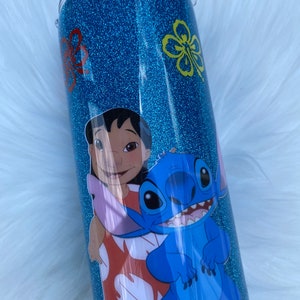 Pu&ograve; includere: Un bicchiere di glitter blu turchese con un'immagine di cartone animato di Stitch e Lilo del film Disney Lilo & Stitch. Il bicchiere ha un coperchio trasparente.