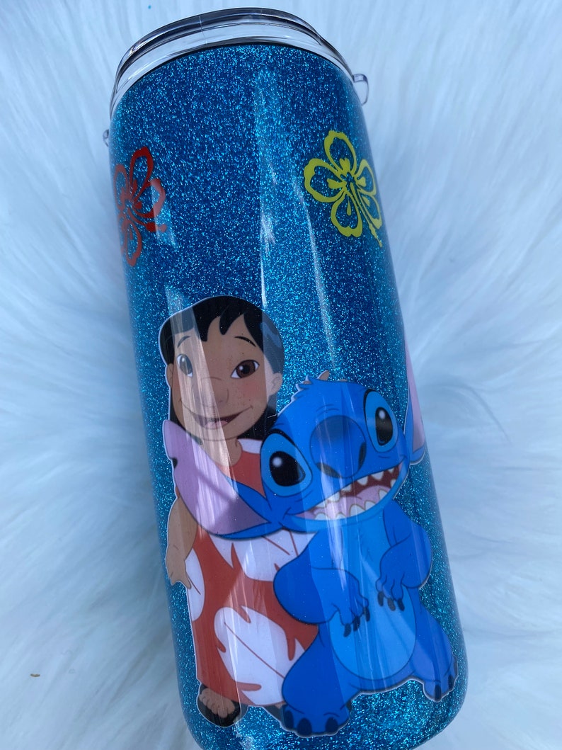 Pu&ograve; includere: Un bicchiere di glitter blu turchese con un'immagine di cartone animato di Stitch e Lilo del film Disney Lilo & Stitch. Il bicchiere ha un coperchio trasparente.