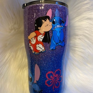 Pu&ograve; includere: Un bicchiere glitterato viola con un'immagine blu e rossa di Stitch e Lilo del film Disney Lilo & Stitch. L'immagine mostra Stitch che bacia Lilo sulla guancia.