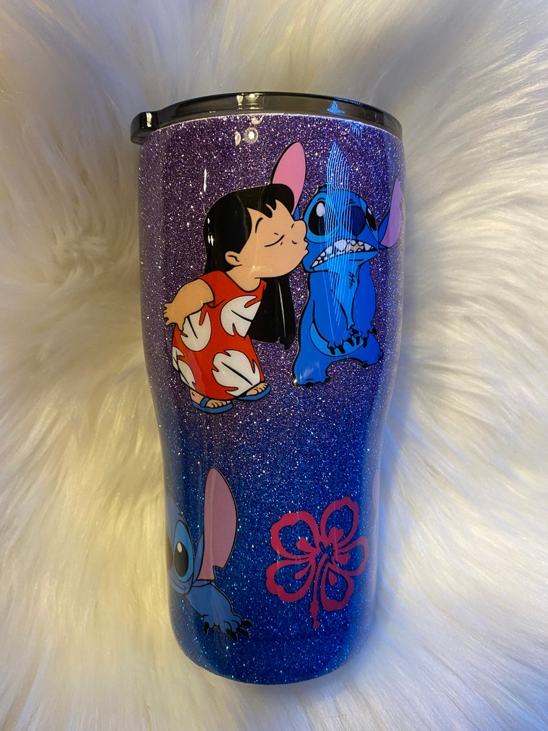Pu&ograve; includere: Un bicchiere glitterato viola con un'immagine blu e rossa di Stitch e Lilo del film Disney Lilo & Stitch. L'immagine mostra Stitch che bacia Lilo sulla guancia.
