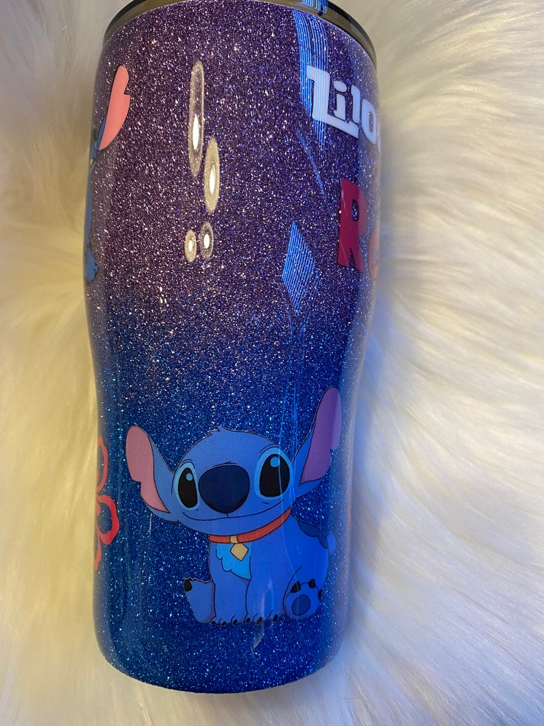 Pu&ograve; includere: Un bicchiere glitter blu e viola con un'immagine di cartone animato di Stitch di Lilo & Stitch. Il bicchiere ha il testo "Lilo" e "Stitch".