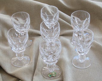 Könnte beinhalten: Sieben klare Kristall-Likörgläser mit Diamantschliffmuster. Jedes Glas hat einen Stielfuß. Die Gläser sind auf einem neutralfarbenen Stoff angeordnet.