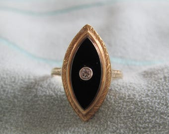 May include: A gold ring featuring a black onyx centre stone and a small diamond. The ring has a leaf-like design around the black stone and a delicate band. The ring is set against a light blue and white background.