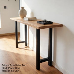 May include: A rectangular wooden console table with black metal legs. The tabletop is light brown, and the legs are a contrasting black. The table is decorated with a vase, books, and a tray with keys. The table is 60 inches long.