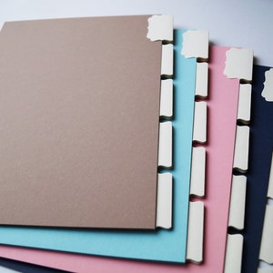 Könnte beinhalten: Ein Satz von vier Trennern mit Laschen in Braun, Blau, Rosa und Dunkelblau. Die Trenner haben weiße Laschen mit abgerundeten Kanten.