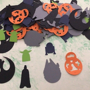 May include: A collection of paper cutouts featuring characters and symbols from Star Wars. The cutouts are in various colors, including black, green, orange, and gray. The characters include Yoda, Darth Vader, R2-D2, and the Death Star. The symbols include the Rebel Alliance symbol and the Imperial symbol.