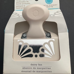 May include: A white and silver Martha Stewart Crafts deep edge punch with a daisy fan design. The punch is packaged in a white box with the Martha Stewart Crafts logo and the text "deep edge punch", "perforador de borde profundo", "poinçon à bord prof", "daisy fan", "abanico de margaritas", and "éventail de marguerites".