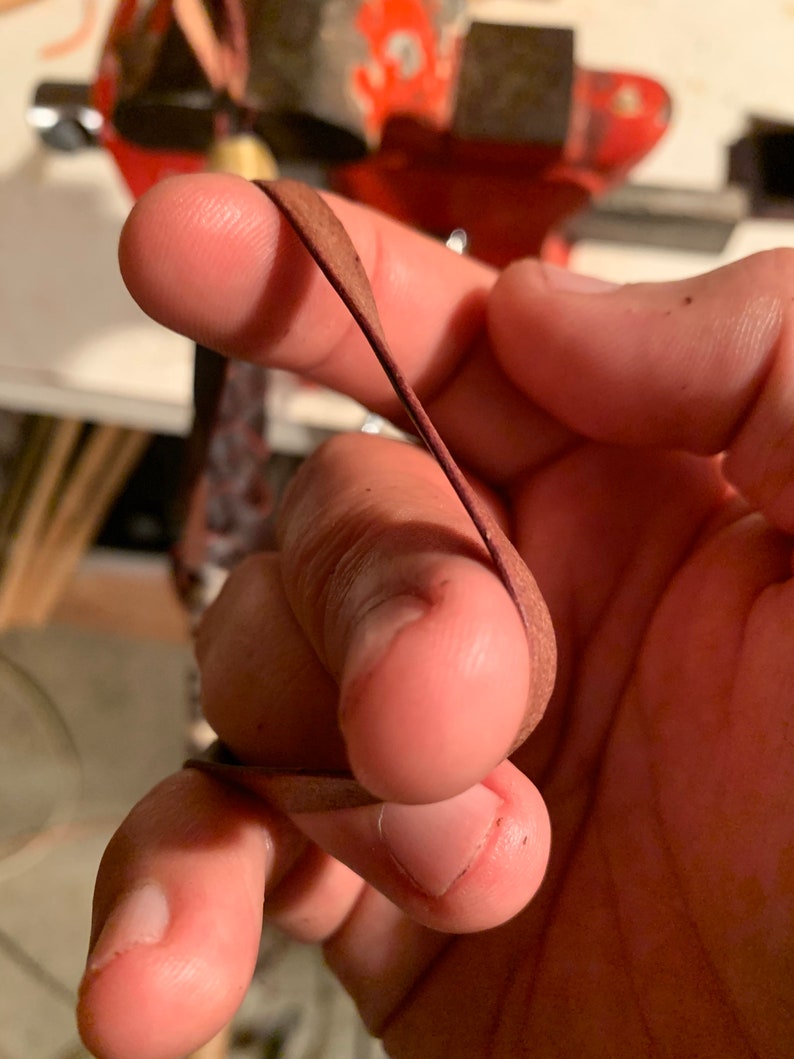 May include: A close-up of a hand holding a thin, brown leather strip. The leather is folded in half and the hand is holding it in place.