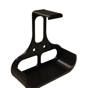 Può includere: Un supporto da parete in plastica nera con un ripiano curvo e un gancio in cima. Il supporto è progettato per contenere un piccolo oggetto, come un telefono o uno spazzolino da denti.
