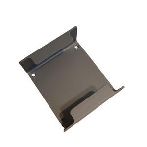 Puede incluir: Un soporte metálico rectangular de color gris oscuro con dos bordes curvos y dos orificios para el montaje. El soporte está diseñado para sujetar un objeto, posiblemente una estantería o un objeto similar.