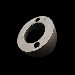 Puede incluir: Un anillo de metal gris con una abertura circular y tres pequeños agujeros. El anillo está ligeramente inclinado y tiene una superficie texturizada.